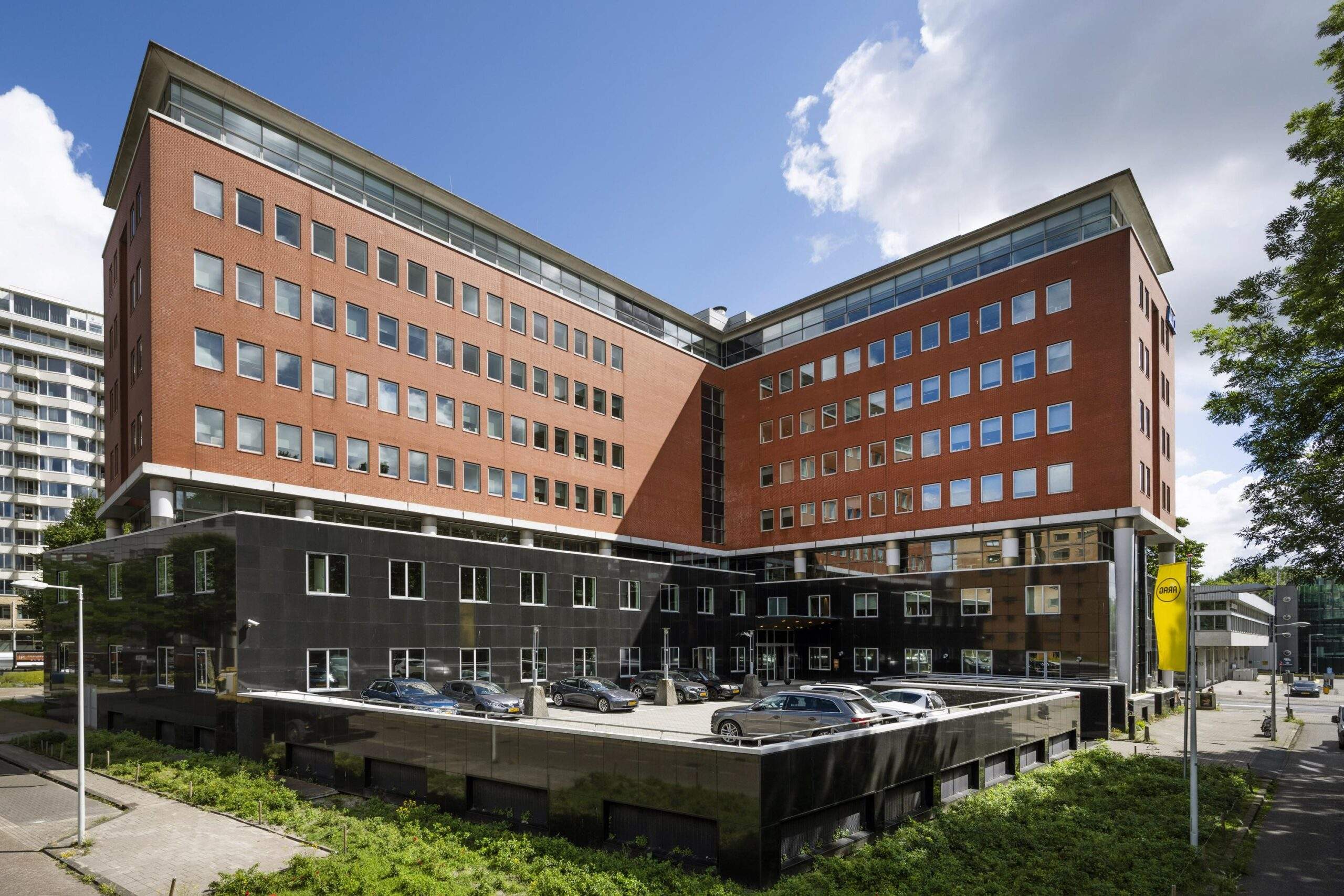 Kantoorpand aan het Koningin Wilhelminaplein in Amsterdam met rode bakstenen gevel en parkeergarage op de voorgrond.